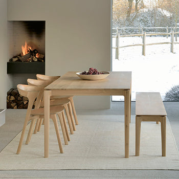 Ethnicraft Bok Esstisch mit passenden Stühlen und Bank aus hellem Massivholz – minimalistisches Esszimmer mit Kamin und Winterlandschaft