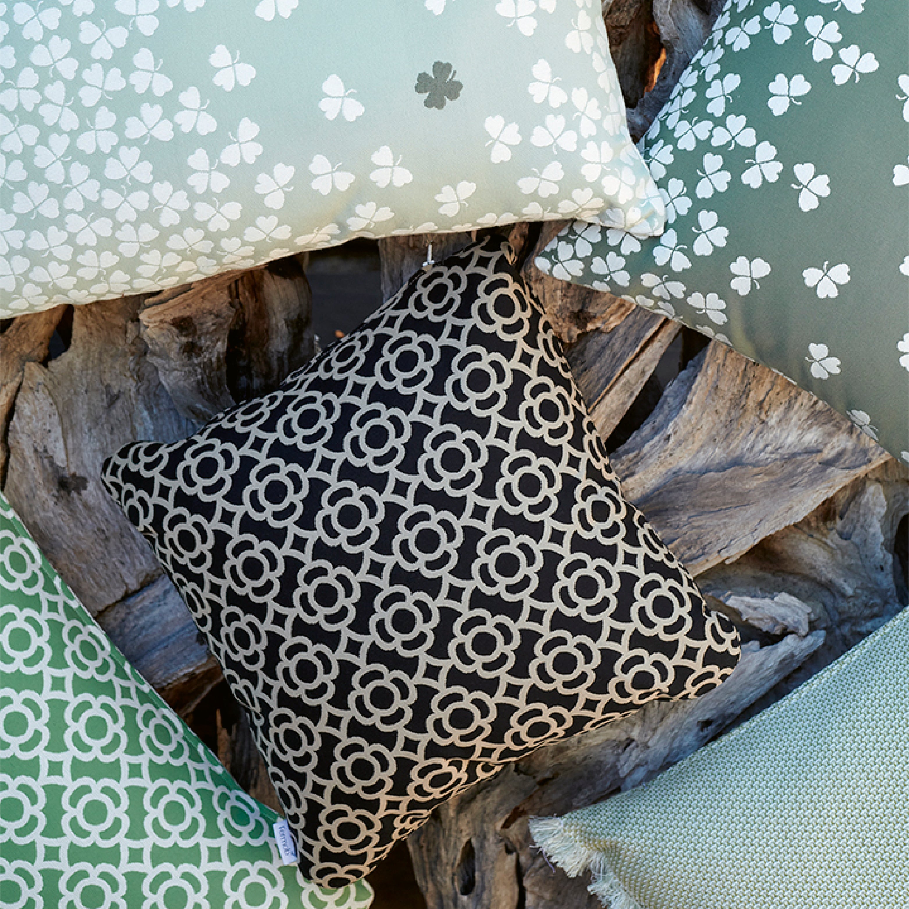 Outdoor-Kissen mit grafischen und floralen Mustern in Grüntönen, arrangiert auf verwittertem Treibholz