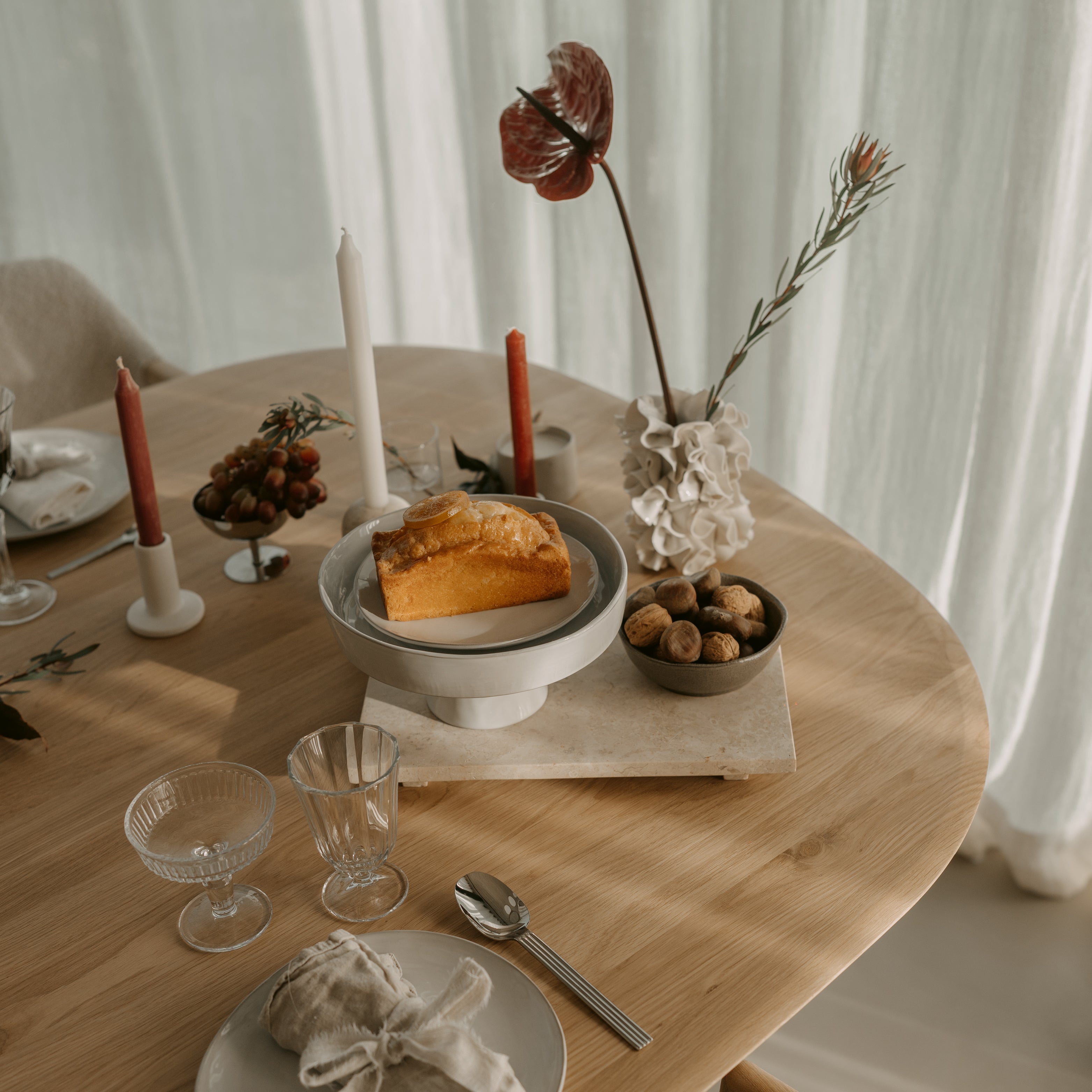 Runder Holztisch mit Kerzen, Brot und Leinenserviette, stilvoll gedeckter Esstisch im sanften Tageslicht
