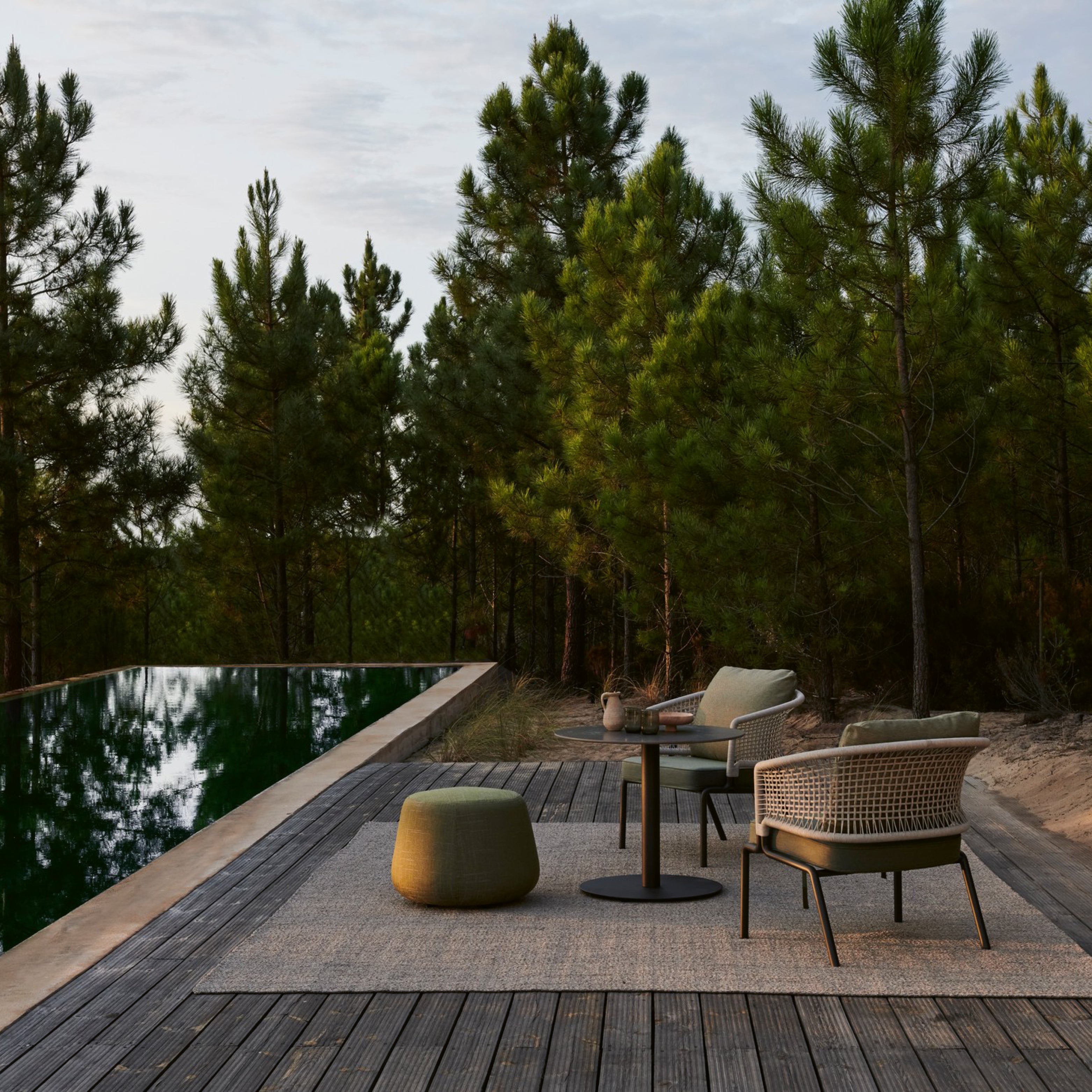 CTR Outdoor-Sessel von Tribù auf Holzdeck am Pool – elegantes Gartenset mit Pouf und Beistelltischen inmitten natürlicher Waldkulisse