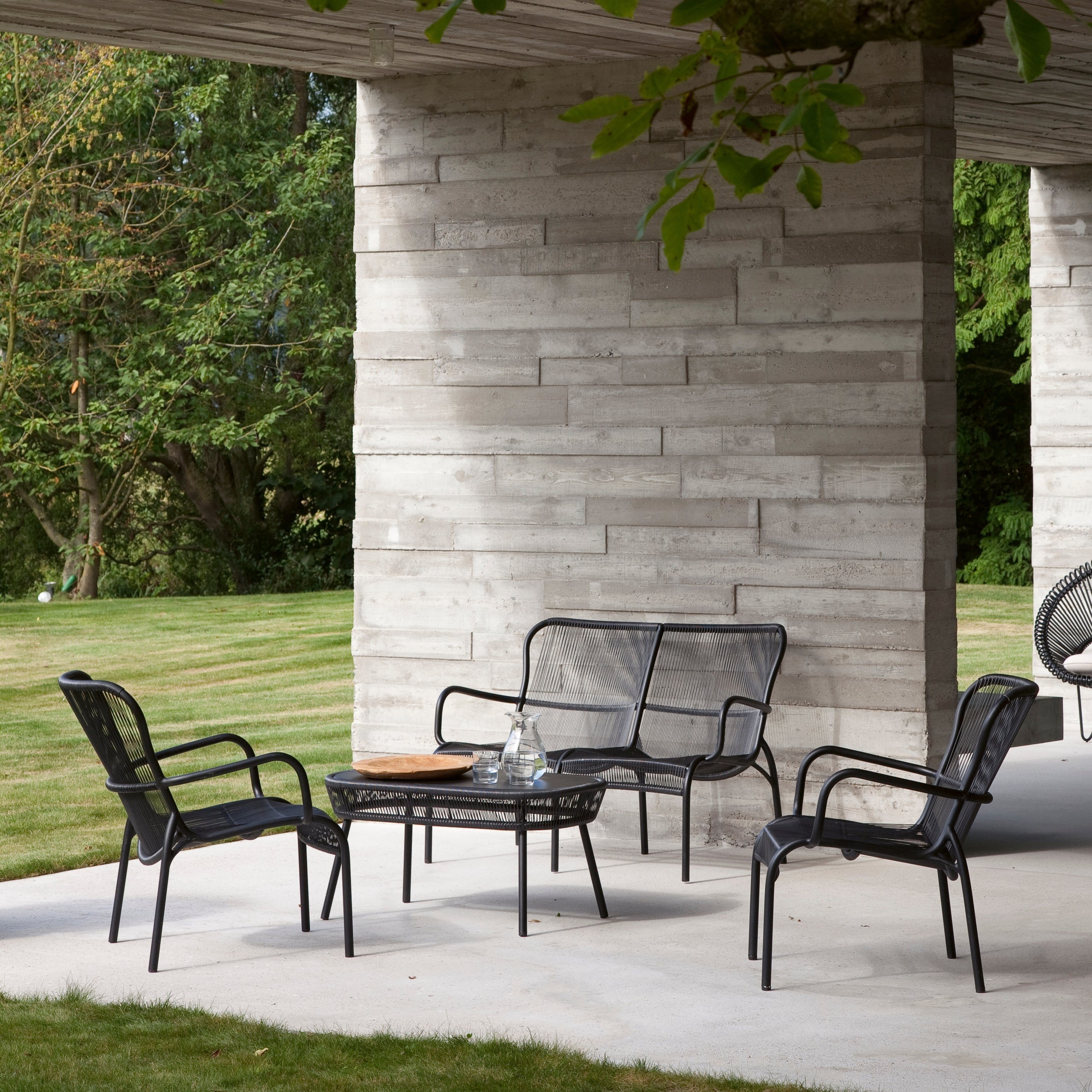 Loop Loungesessel und 2-Sitzer Bank aus schwarzem Seilgeflecht von Vincent Sheppard unter Betonvordach