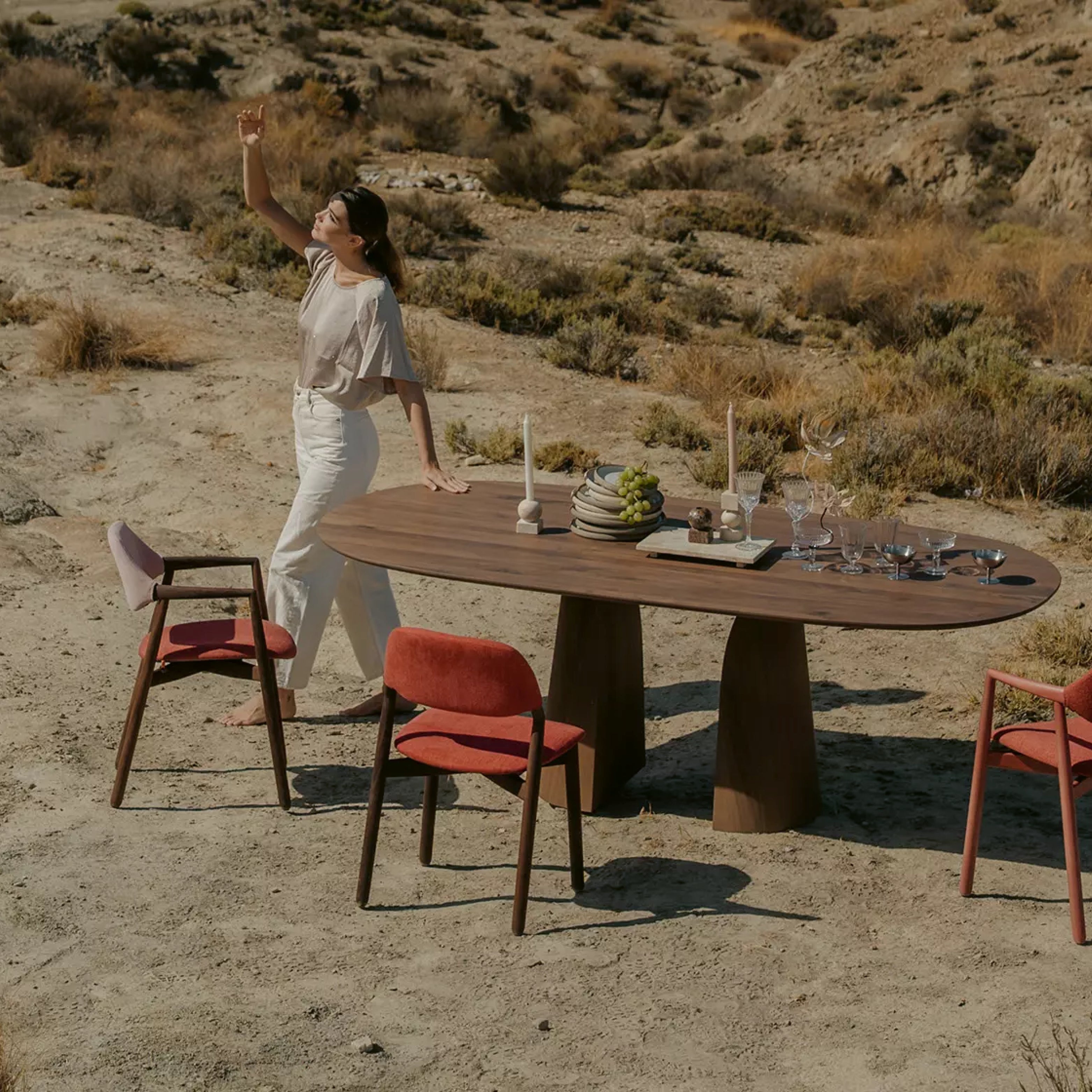 Design-Essgruppe von Mobitec mit ovalem Holztisch und farbigen Polsterstühlen in einer eindrucksvollen Wüstenlandschaft inszeniert.