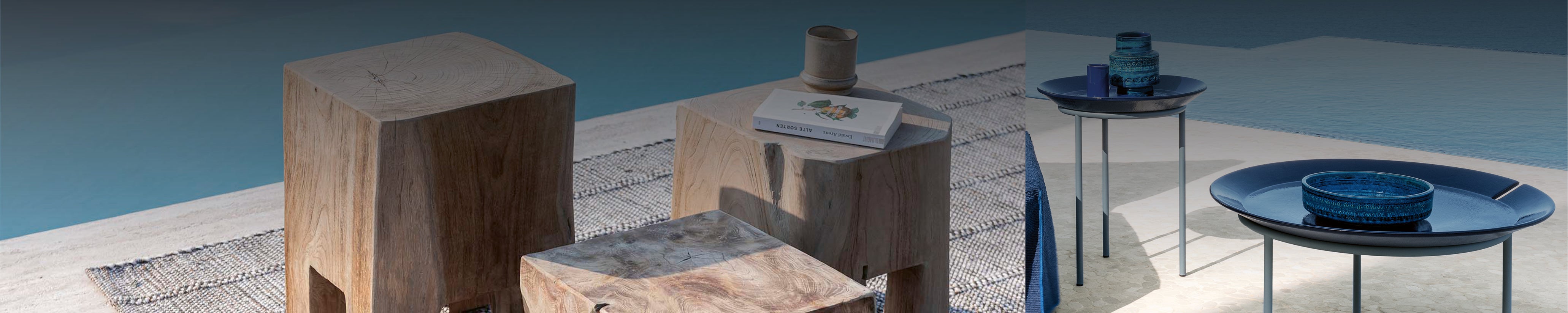 Zwei Stilrichtungen von Outdoor-Beistelltischen auf heller Terrasse mit Meerblick: links kubische Massivholztische mit natürlicher Struktur, rechts filigrane Gervasoni Tische mit blauen Keramikplatten und dekorativen Gefäßen – stilvoll arrangiert auf Teppich und Steinboden.