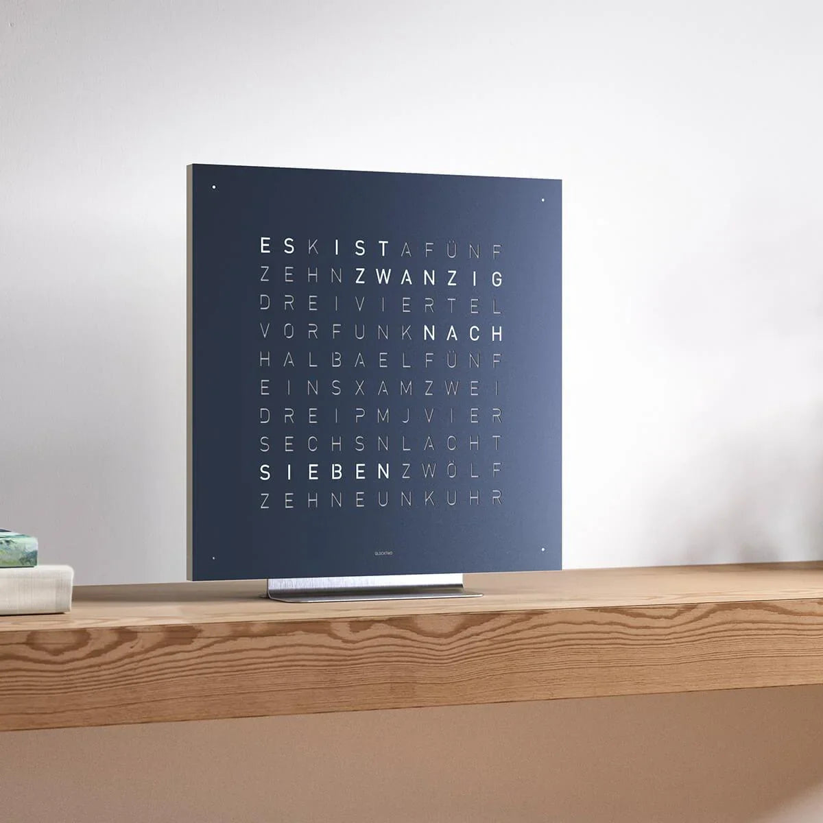 QLOCKTWO Earth 45 in Midnightblau auf Edelstahl-Standfuß mit weißer Halterung – stilvolle Beispieleinrichtung im modernen Ambiente mit ikonischer Wortuhr