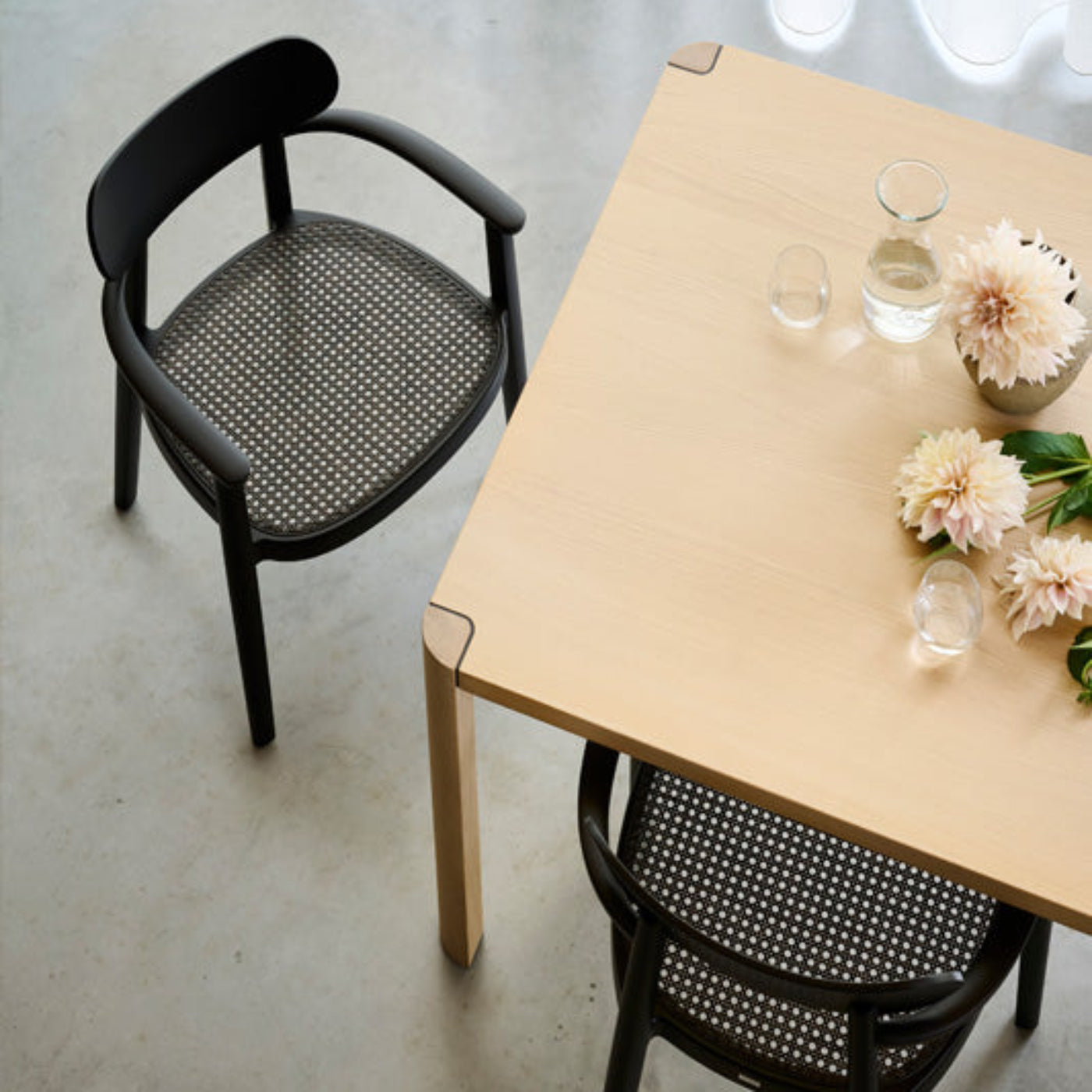 Schwarze Thonet Bugholz-Armlehnstühle mit Wiener Geflecht an einem hellen Holztisch.