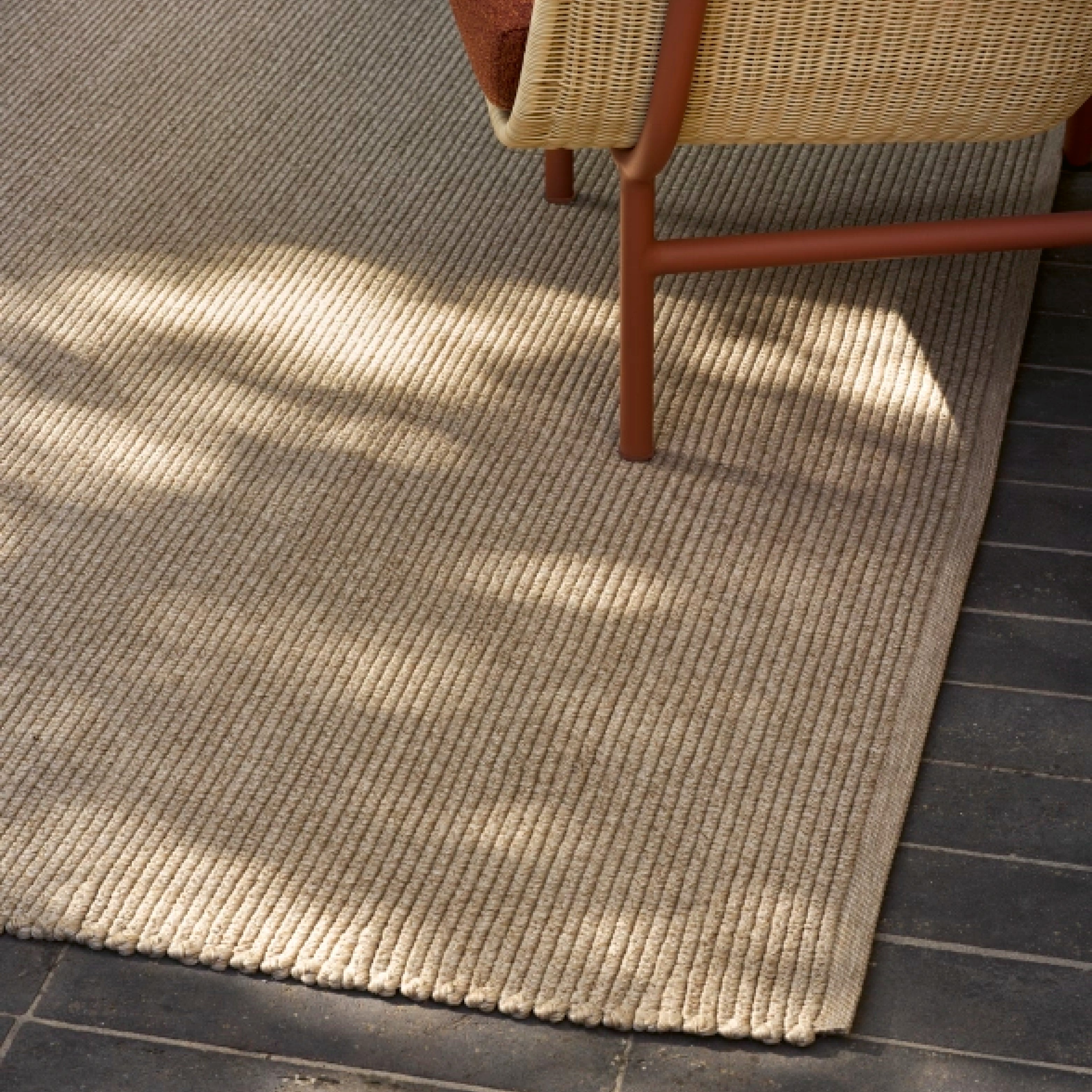 Beiger Outdoor Teppich mit strukturierter Oberfläche auf dunklem Steinboden – ideal für Terrasse oder Balkon.