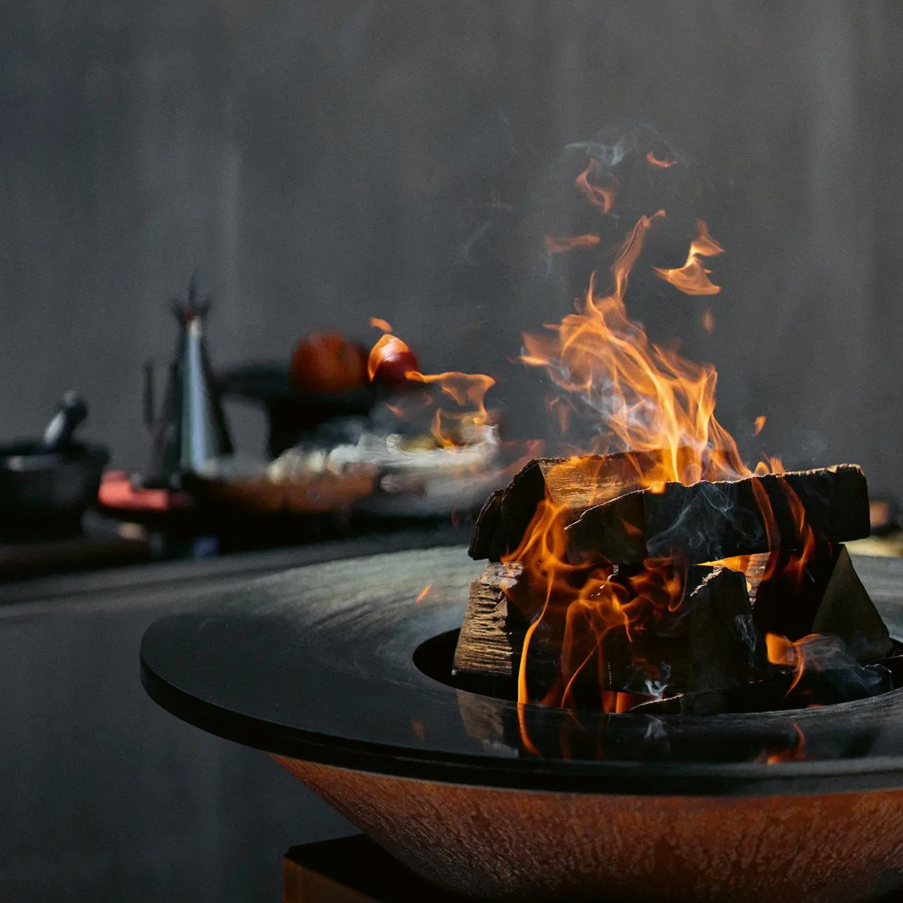 OFYR Grill mit loderndem Holzfeuer auf edler Feuerplatte – stimmungsvolle Outdoor-Küche mit Fokus auf Design und Geselligkeit.