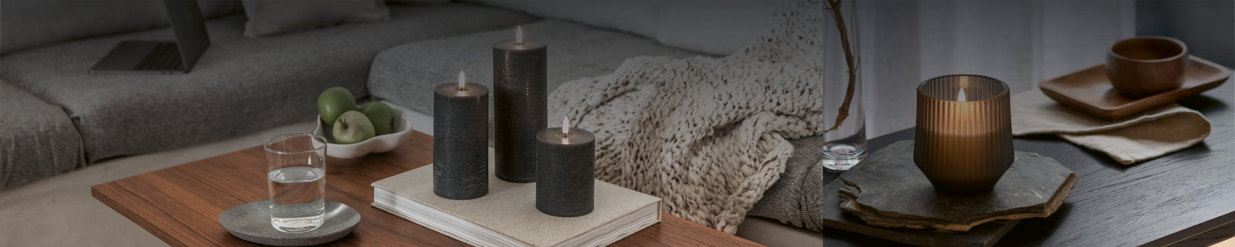 Elegante LED-Kerzen in graue Echtwachsoptik, andere in Glass mit flackerndem Licht auf einem nordischen Holztablett im Wohnambiente.